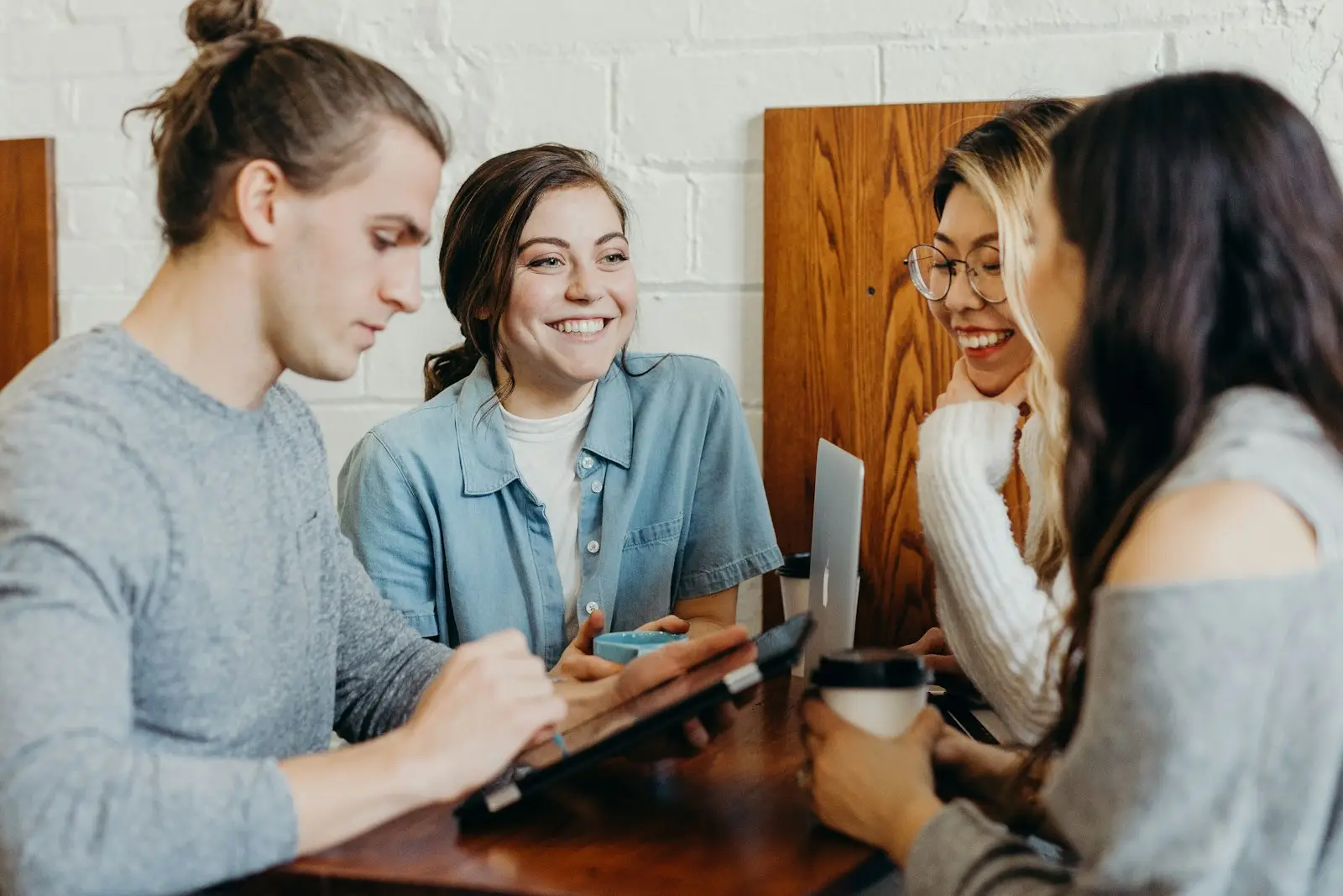 Four friends laughing around a café table with notebooks and coffee
